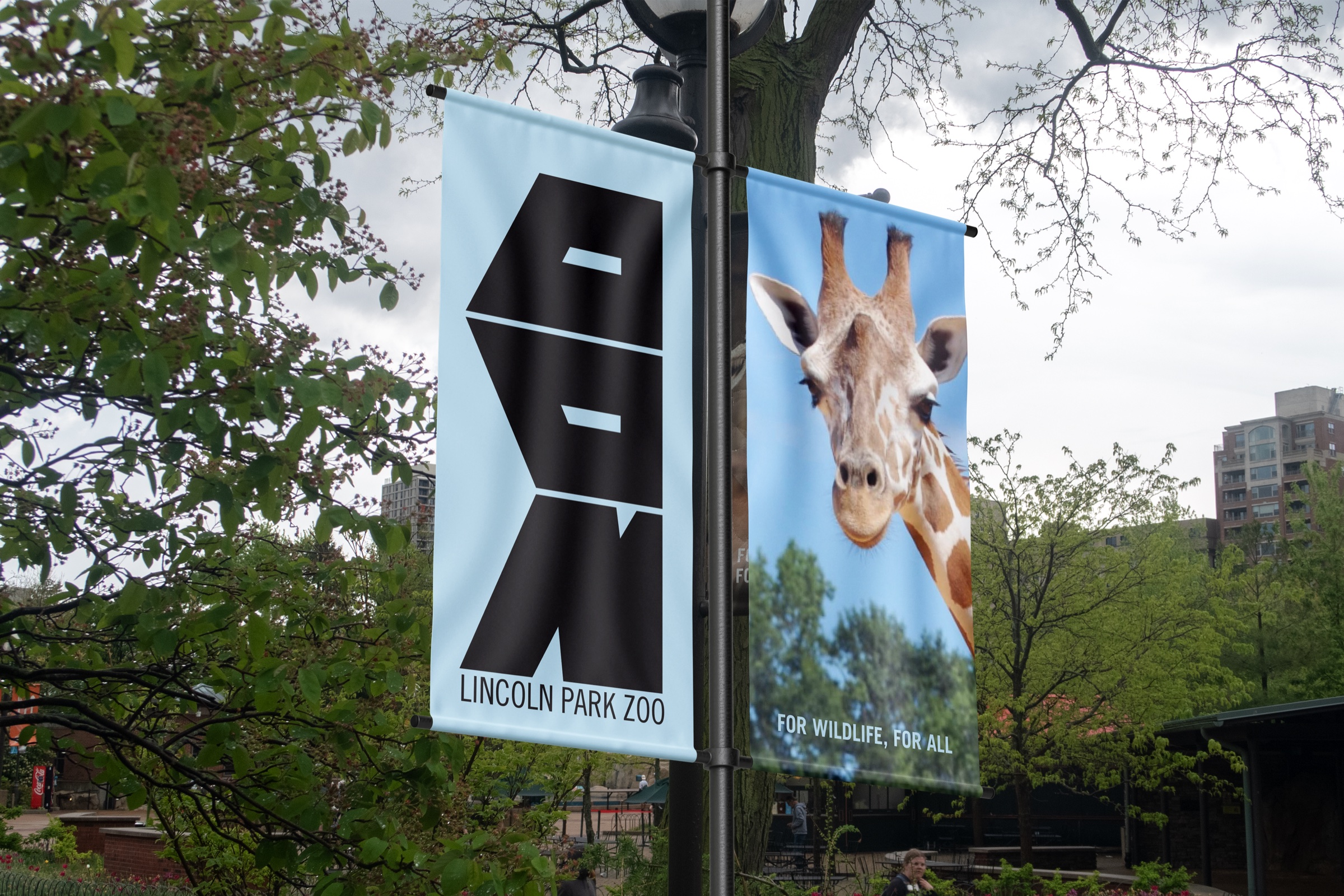 Light blue ZOO banner and giraffe banner on a lamppost among trees
