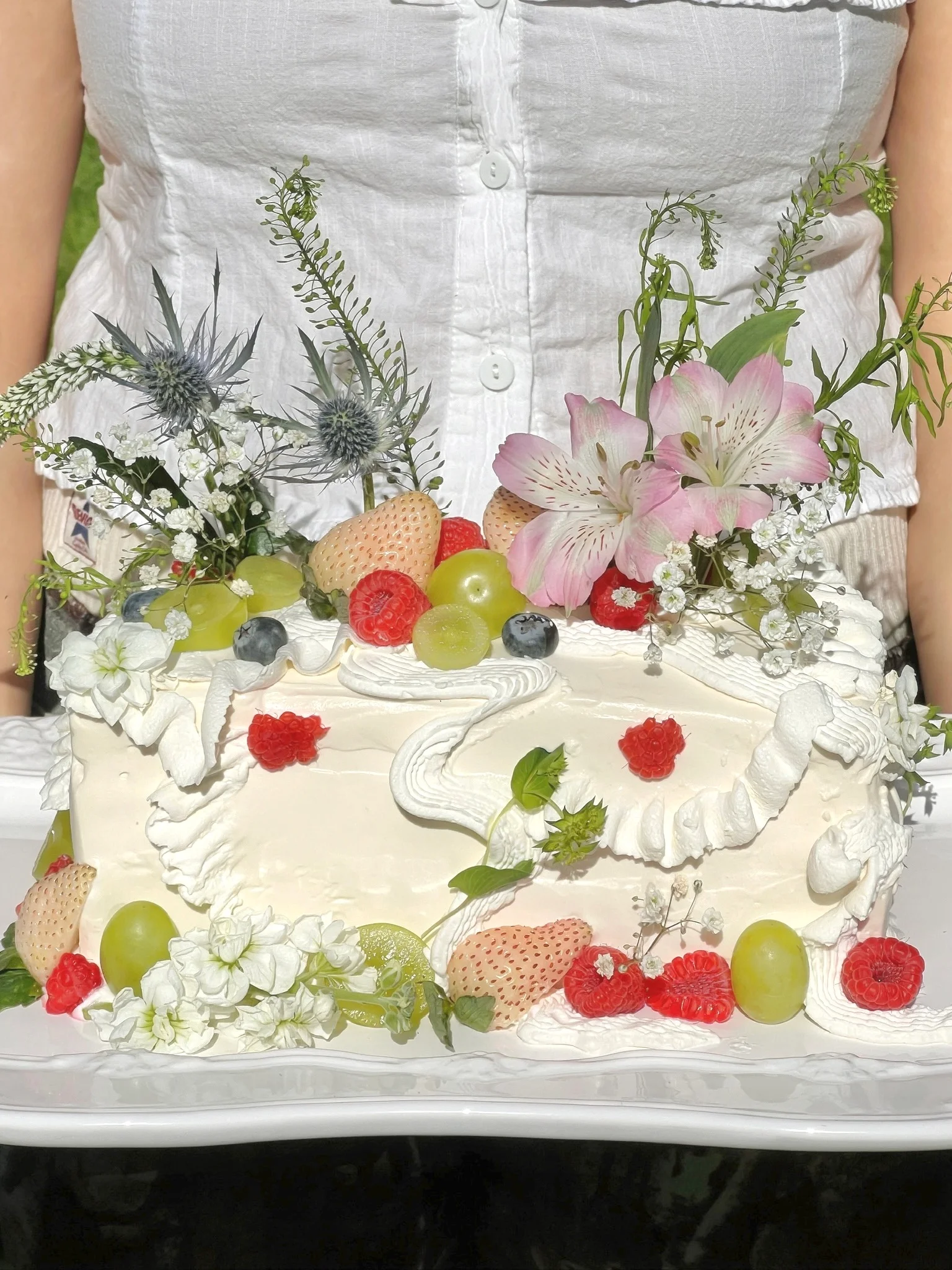 Cake decorated with flowers and fruit, held up outdoors