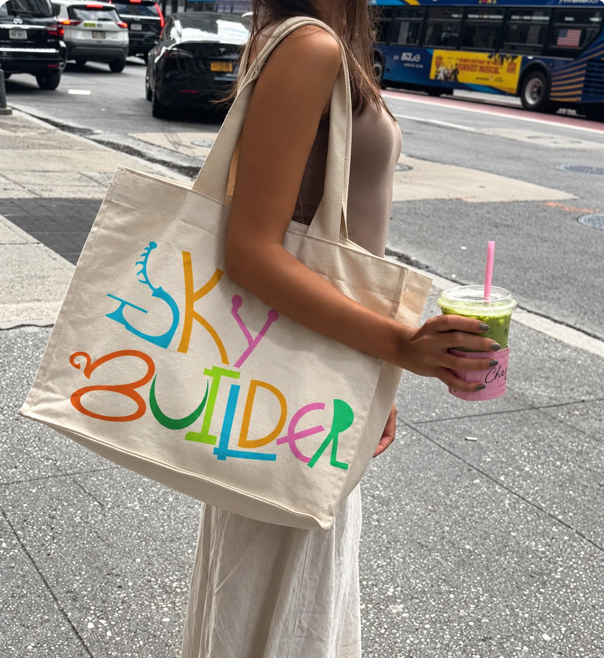 A person on a city street carrying the Sky Builder canvas tote bag