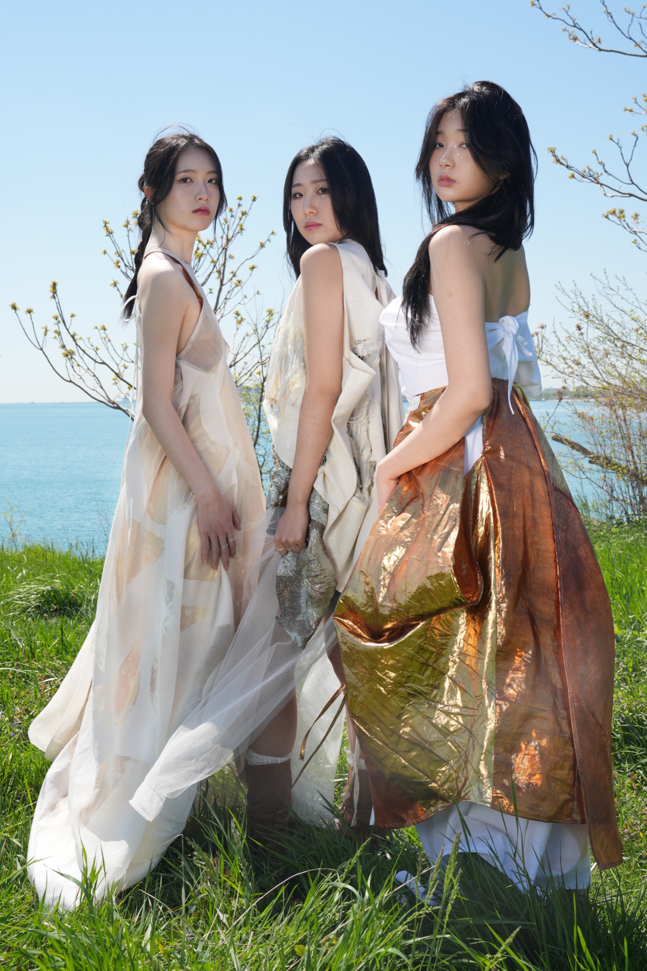 Three models in June Kim's pale draped dresses on the grass by Lake Michigan